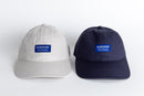 Front view of two Avelamer Bridgeway Capa in Mainsail (off-white) and Deepwater (navy) with navy Avelamer woven brand labels on the cap front panels 