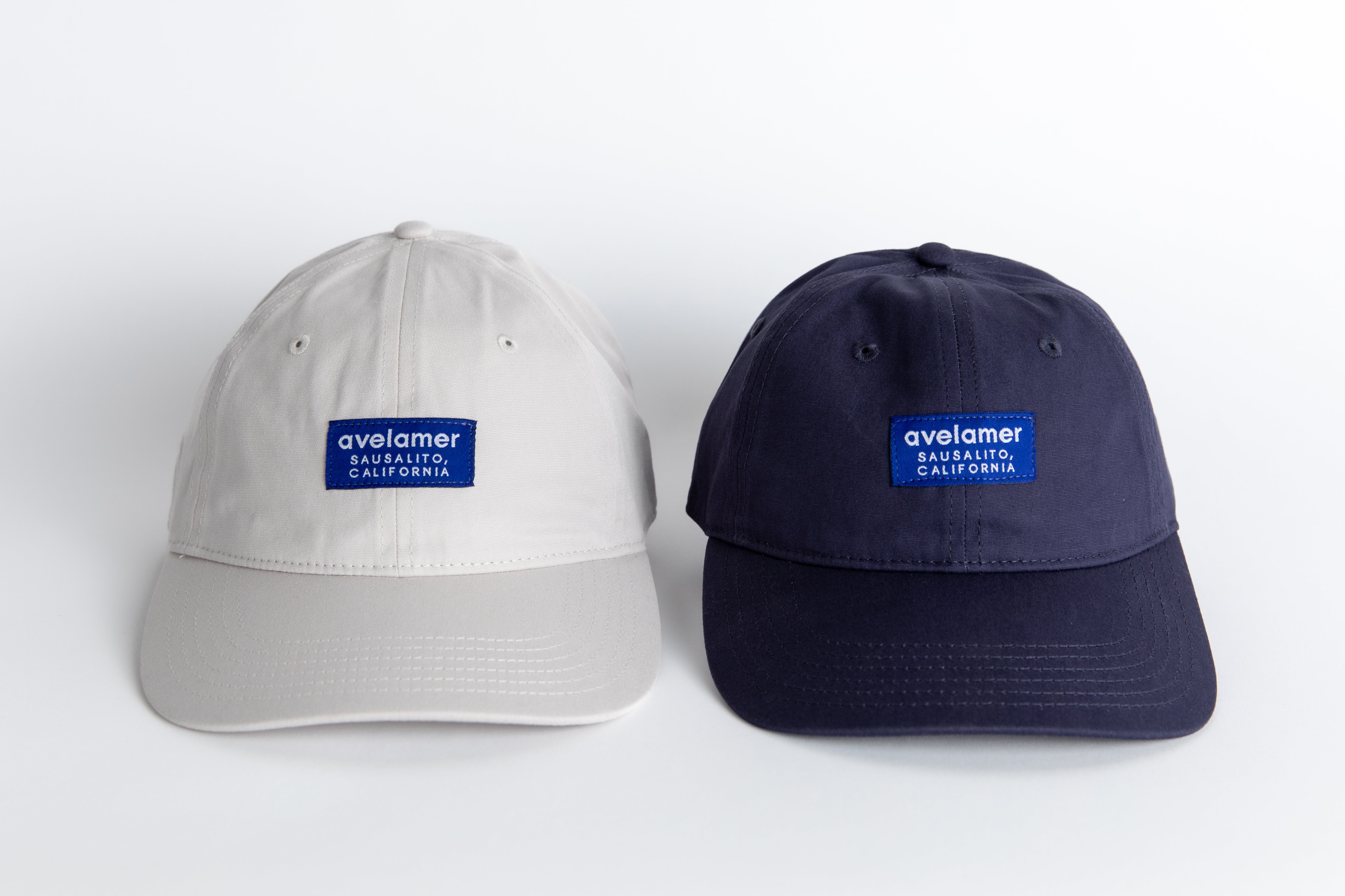 Front view of two Avelamer Bridgeway Capa in Mainsail (off-white) and Deepwater (navy) with navy Avelamer woven brand labels on the cap front panels 