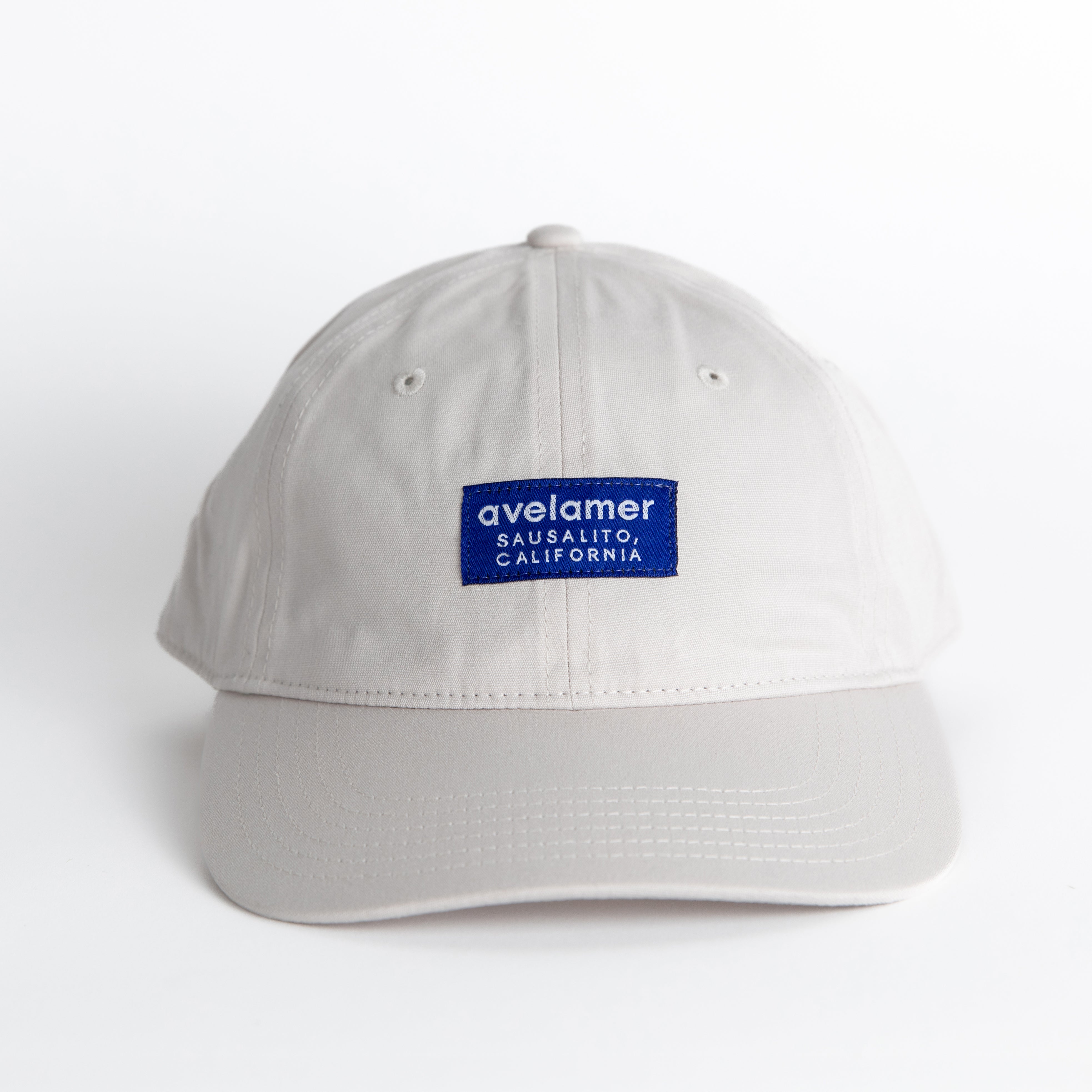 Front view of an Avelamer Bridgeway Cap in Mainsail (off-white) with a navy Avelamer brand woven label on the front panel