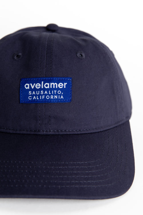 Detail view of an Avelamer Bridgeway Cap in Deepwater (navy) with a tonal Avelamer brand woven label on the front panel