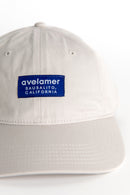Detail view of an Avelamer Bridgeway Cap in Mainsail (off-white) with a navy Avelamer brand woven label on the front panel