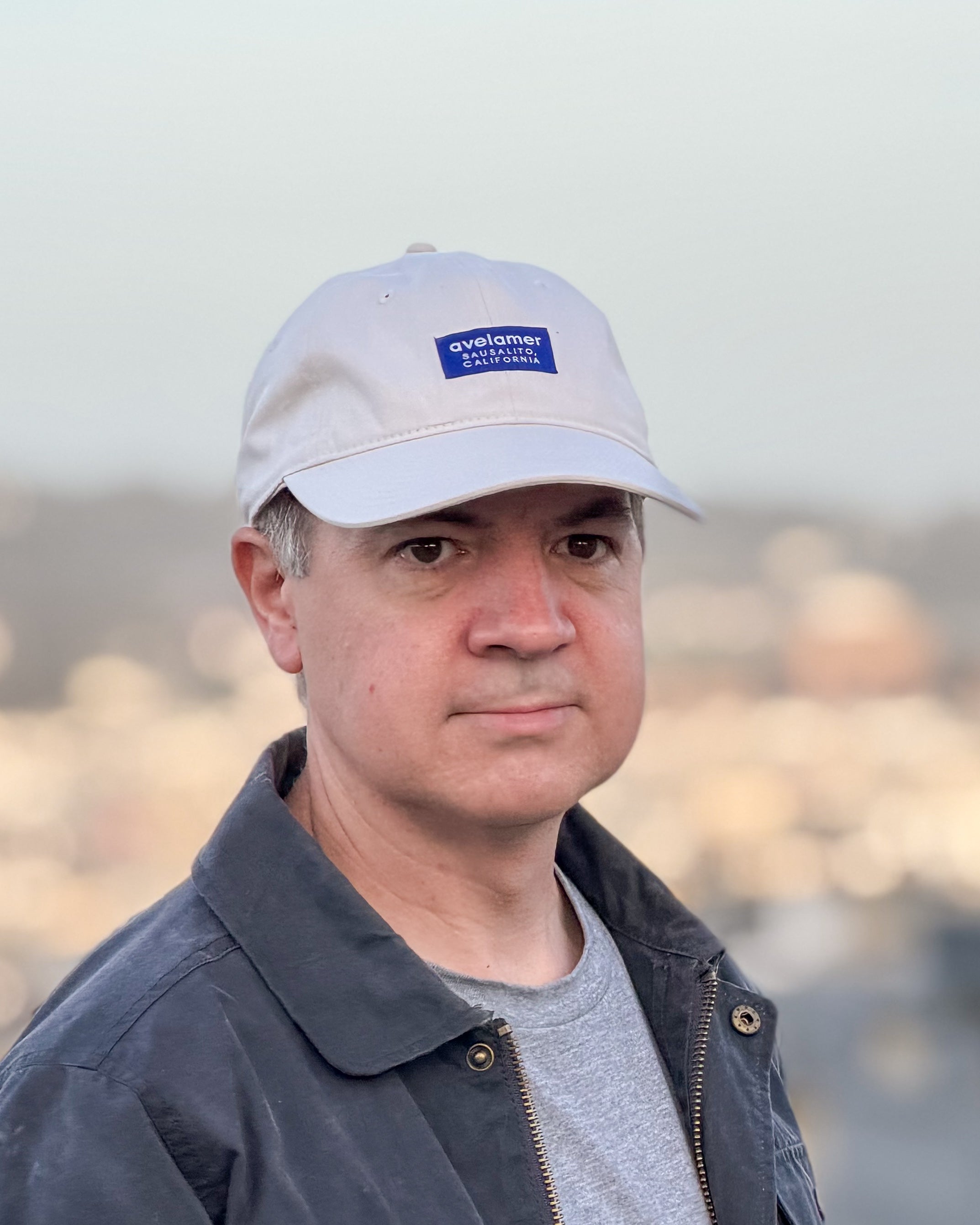 Man wearing an Avelamer Bridgeway Cap in Mainsail (off-white) with navy Avelamer woven brand label on the front