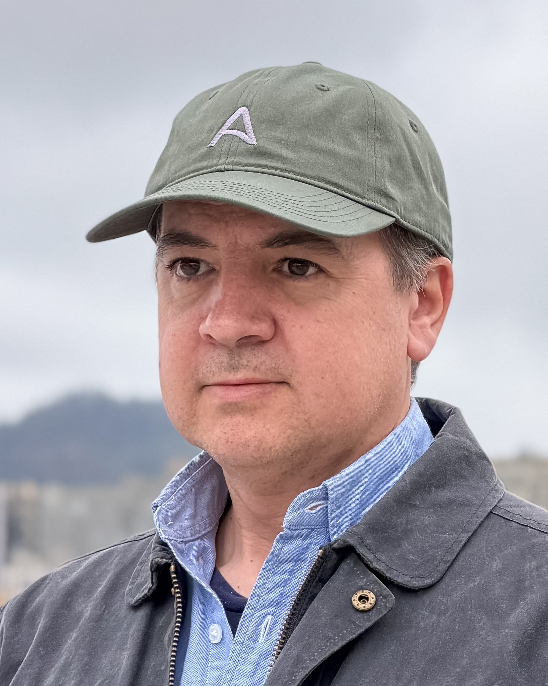 Man wearing a green cap with an embroidered a-flag logo and a blue-gray jacket outdoors