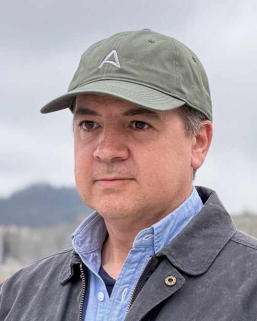 Man wearing a green cap with an embroidered a-flag logo and a blue-gray jacket outdoors