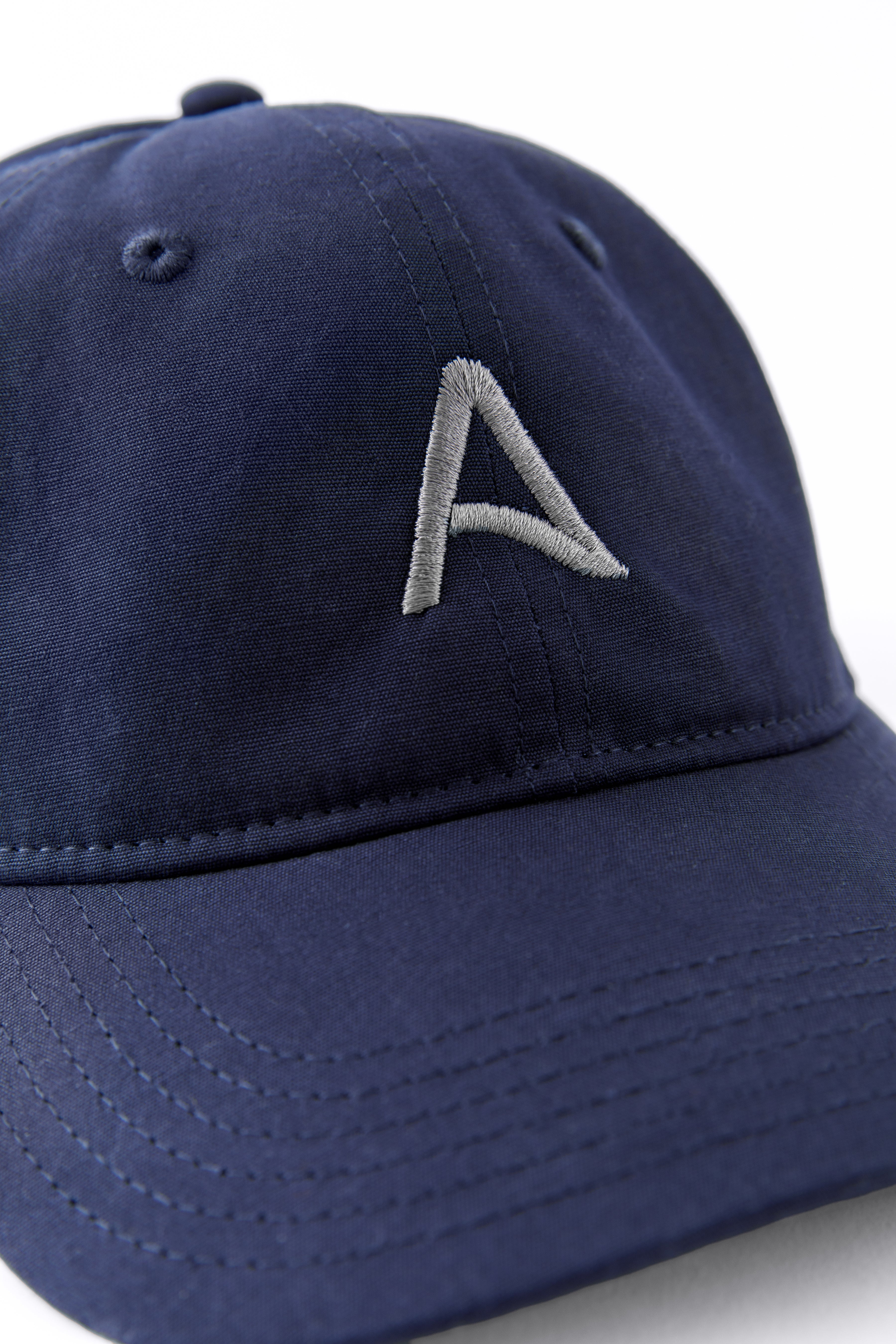 Front view of an Avelamer Caledonia Cap in Deepwater navy with embroidered gray A-flag logo on a white background