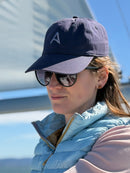Woman wearing an Avelamer Caledonia Cap in Deepwater navy with an embroidered gray A-flag logo on the front