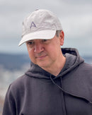 Man wearing the Avelamer Caledonia Cap in Mainsail, an off-white dad cap with embroidered A logo on the crown, paired with a charcoal hoodie.