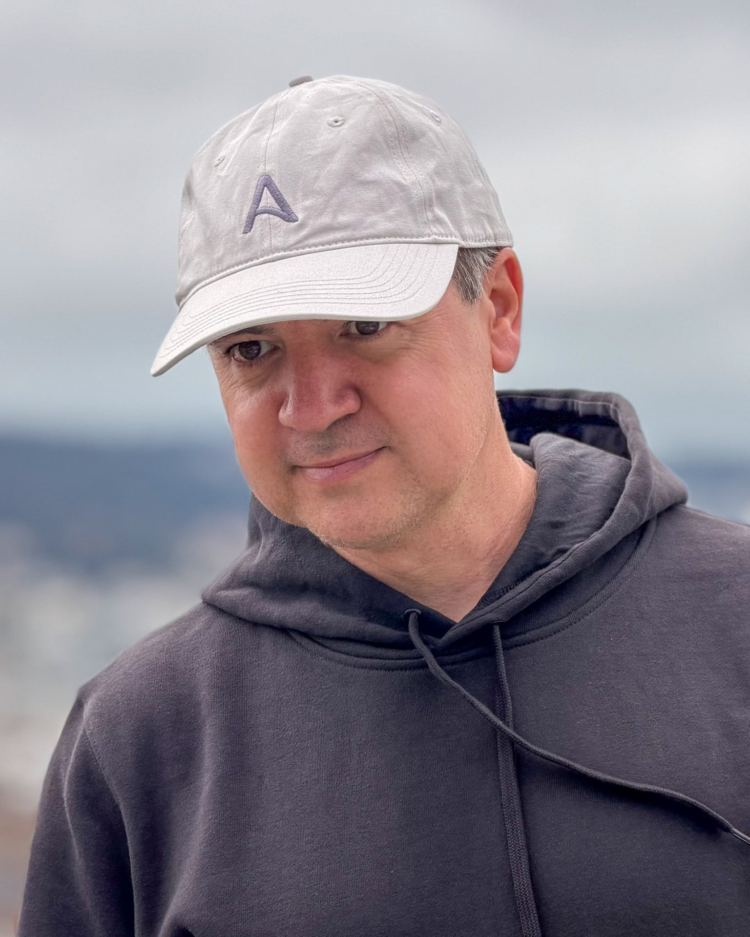 Man wearing the Avelamer Caledonia Cap in Mainsail, an off-white dad cap with embroidered A logo on the crown, paired with a charcoal hoodie.