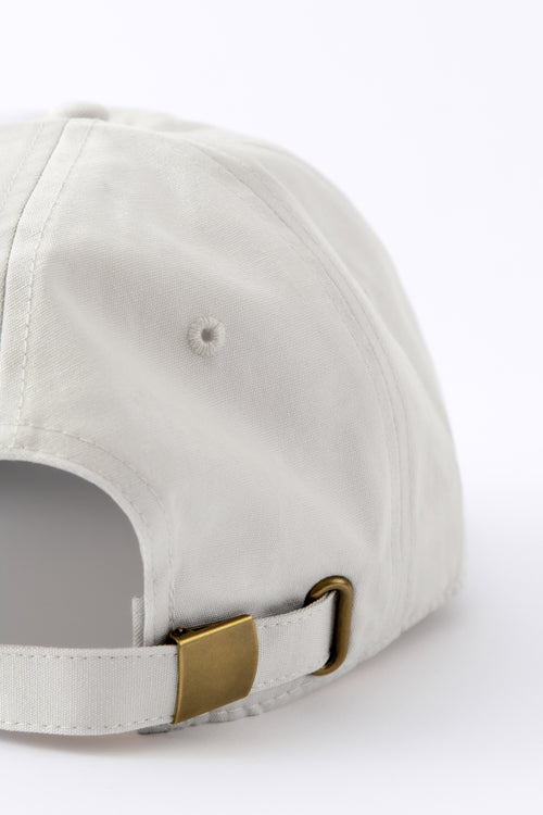 Back view of an Avelamer Caledonia Cap in Mainsail off-white with a gold buckle on a white background