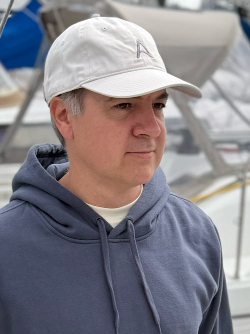 Man wearing an embroidered off-white cap and blue-gray hoodie in a marina