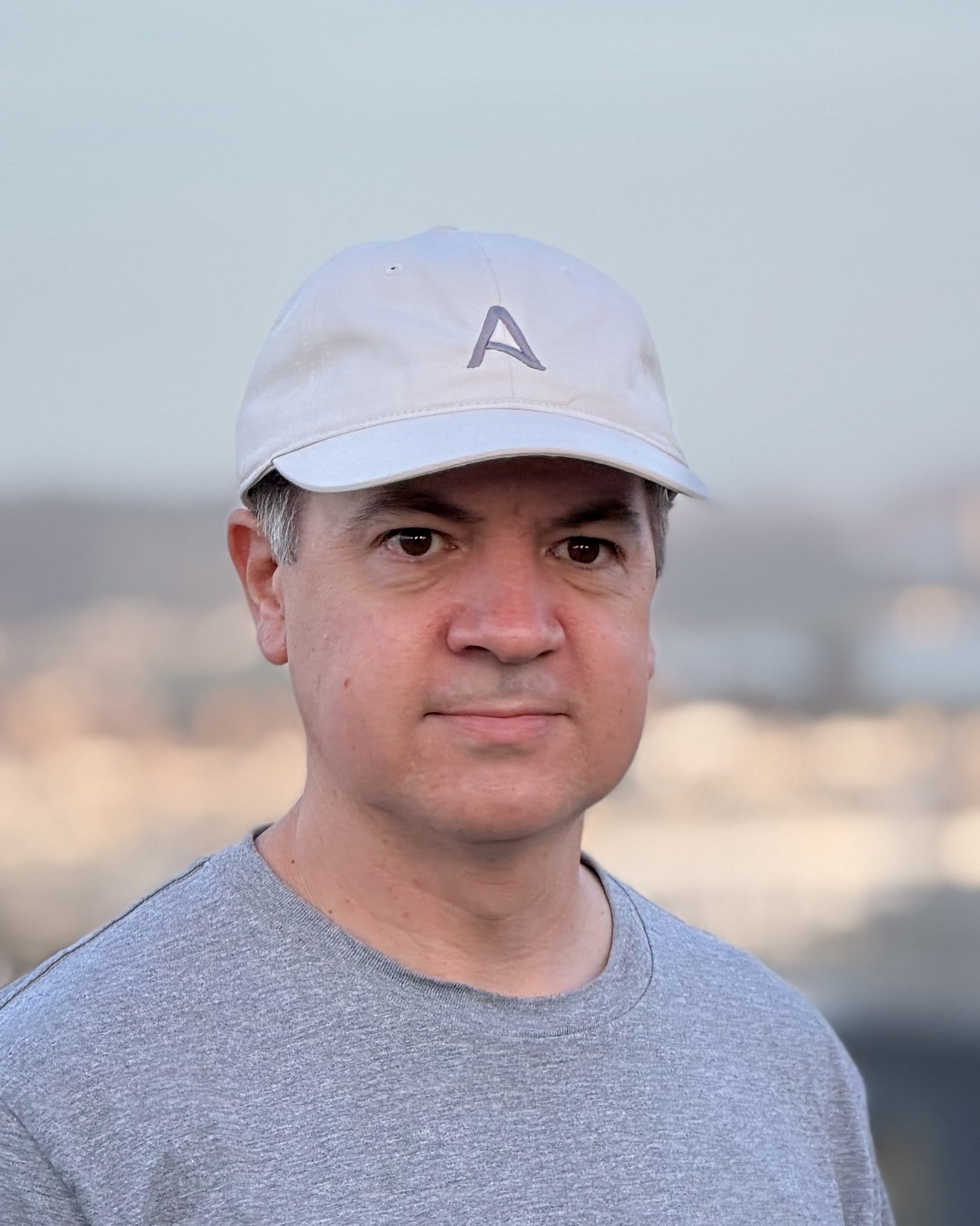 Man wearing an Avelamer Caledonia Cap in Mainsail (off white) cap with an embroidered Avelamer A-flag logo on the front panel, with a blurred background