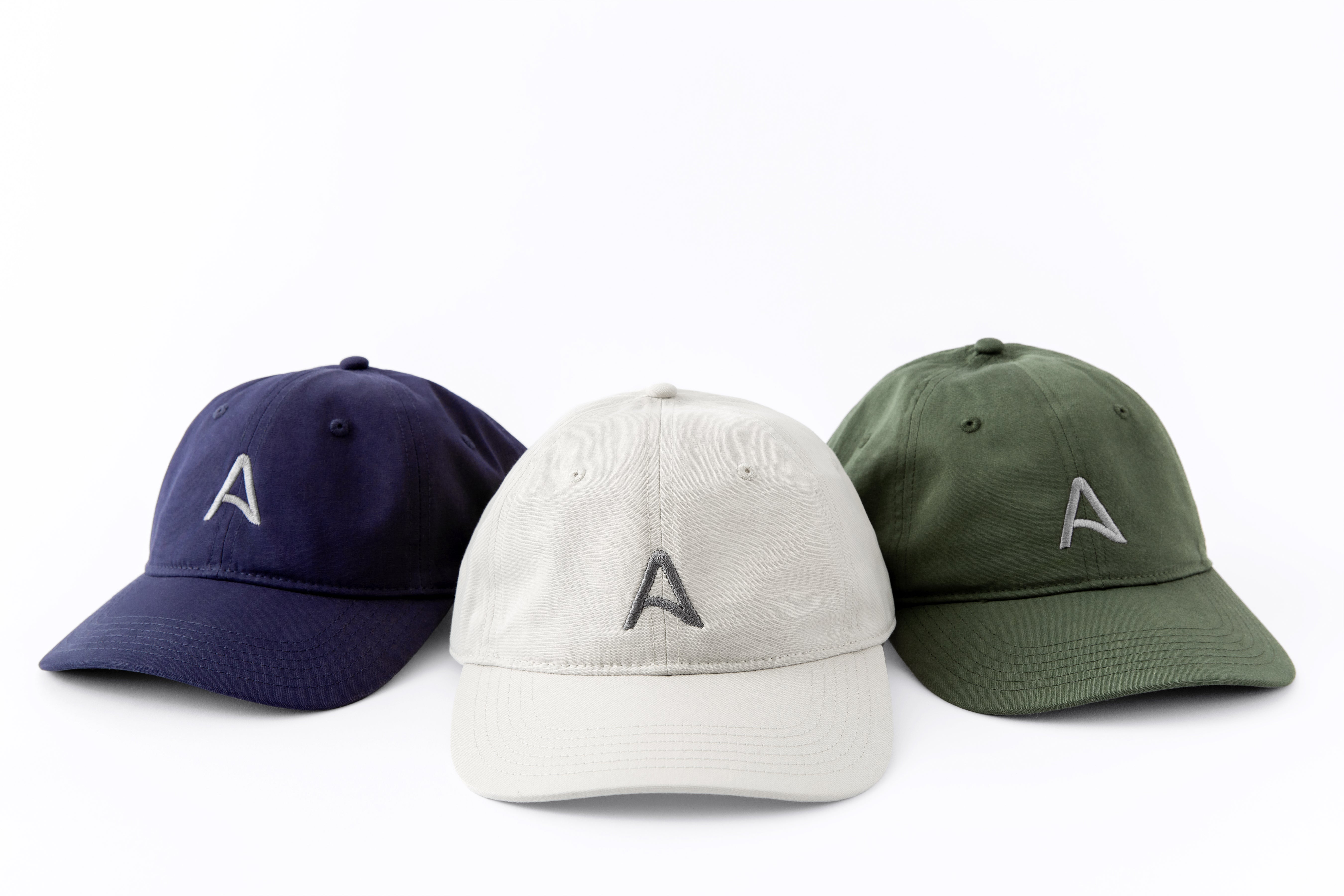 Trio of Avelamer Caledonia Caps in Deepwater navy, Mainsail off-white, Cypress Grove green with gray embroidered A-flag logos visible against a white background.