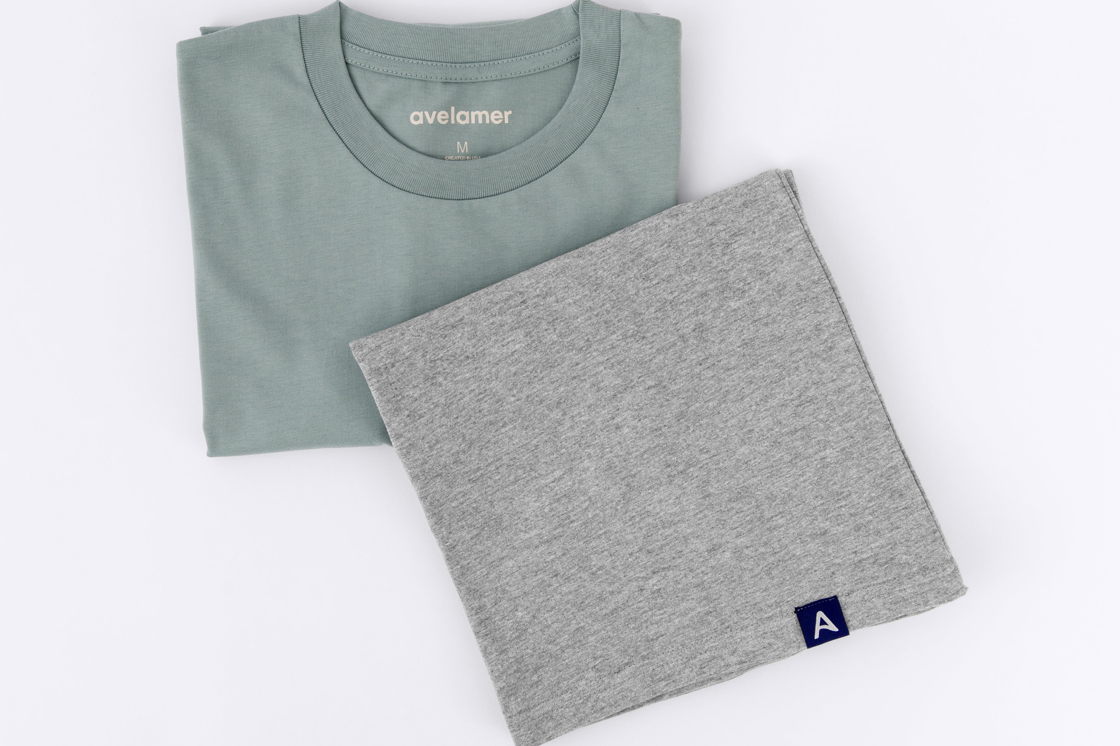 Folded blue-green and heather gray tees with woven A-flag brand hem labels on a white background.
