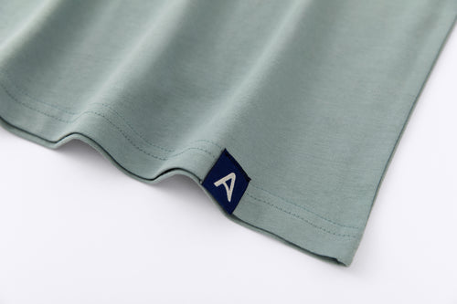 Close-up of Avelamer Ebbide Tee in Shallow Bay blue-green with blue A-flag logo woven hem label