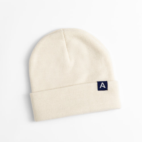 Avelamer Harbor Beanie in Mainsail off-white with blue A-flag logo woven cuff label laid flat on a white background