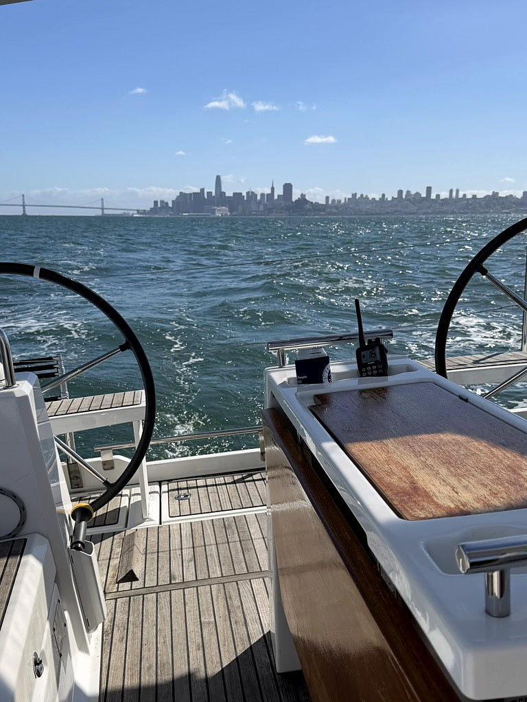 Sailboat cockpit on San Francisco Bay, teak deck and twin wheels, the city skyline across the water.