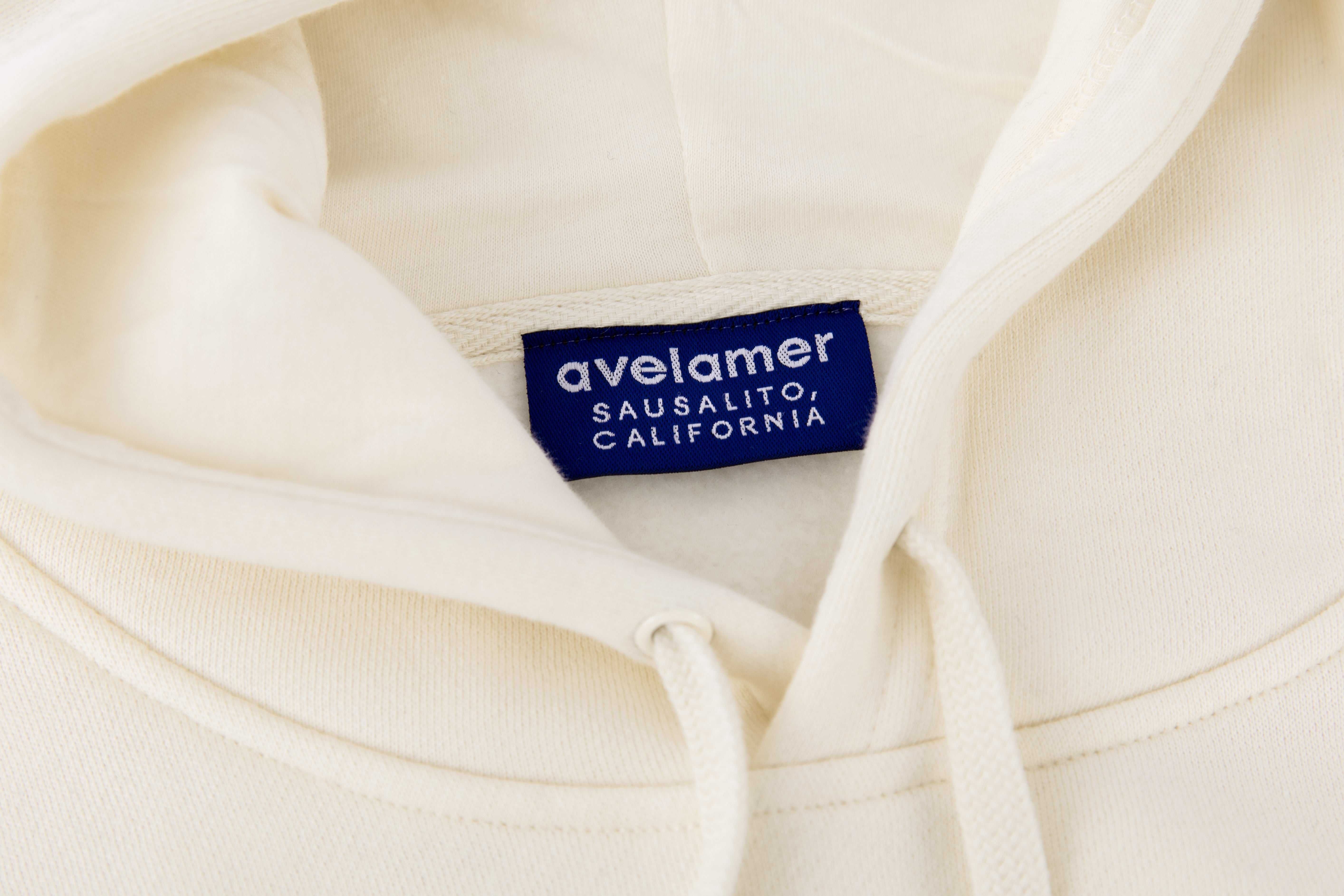Close-up of Avelamer Sausalito Hoodie in Mainsail off-white with a blue woven branded neck label