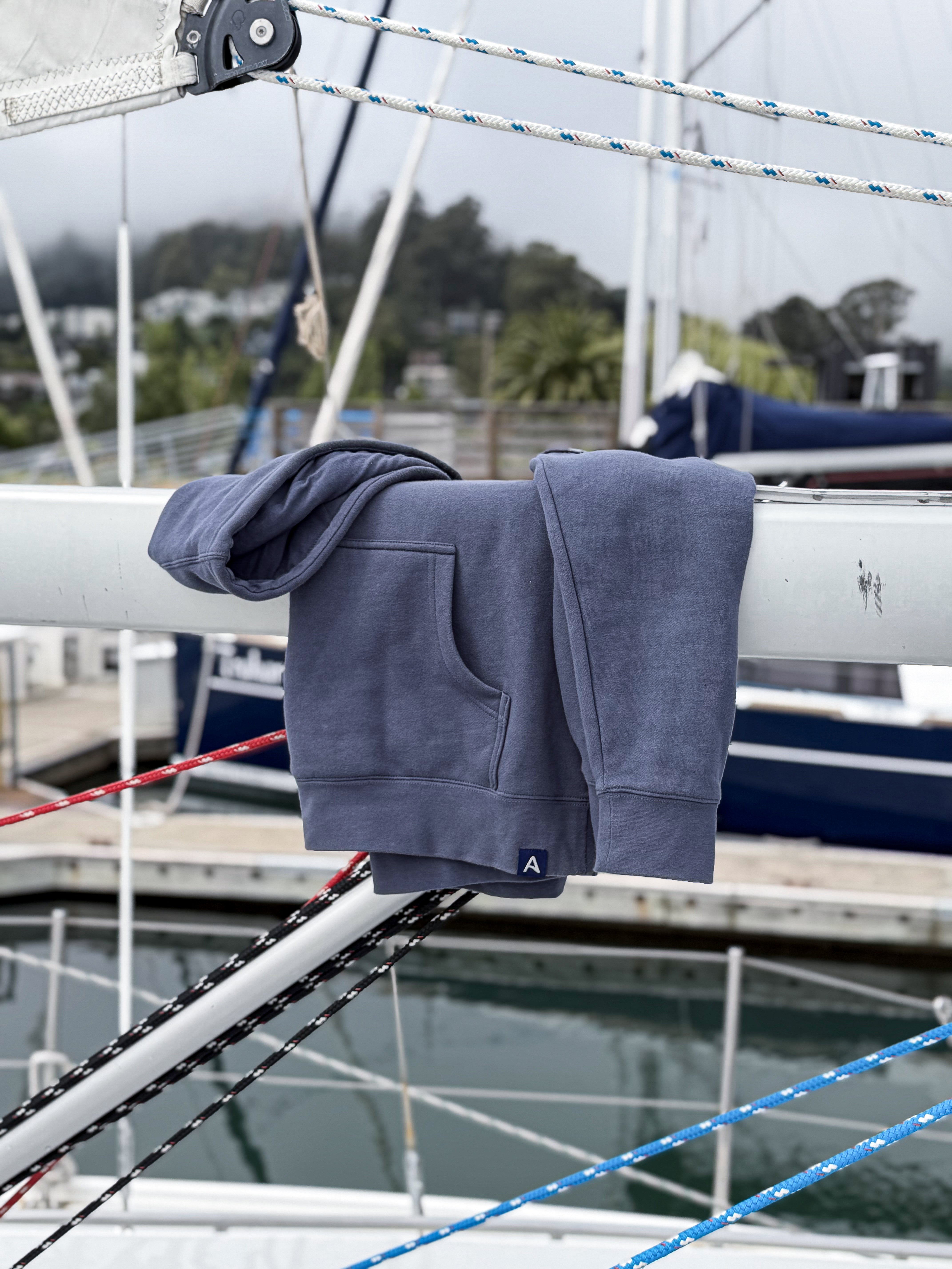 Blue-gray hoodie draped over sailboat boom with marina and boats in the background