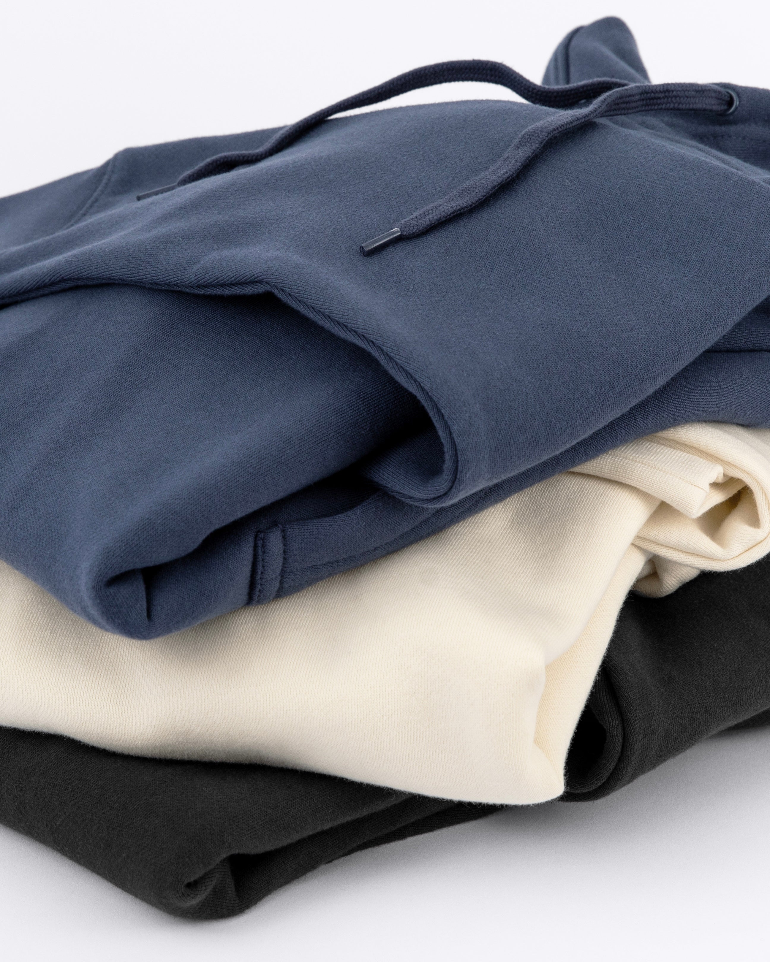 Stack of three Avelamer Sausalito Hoodies in Ocean Slate blue-gray, Mainsail off-white, Headland Shadow dark gray against a white background