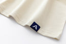 Close-up of Avelamer Spencer Long Sleeve tee in Mainsail off-white with a blue Avelamer A-flag woven hem label. 