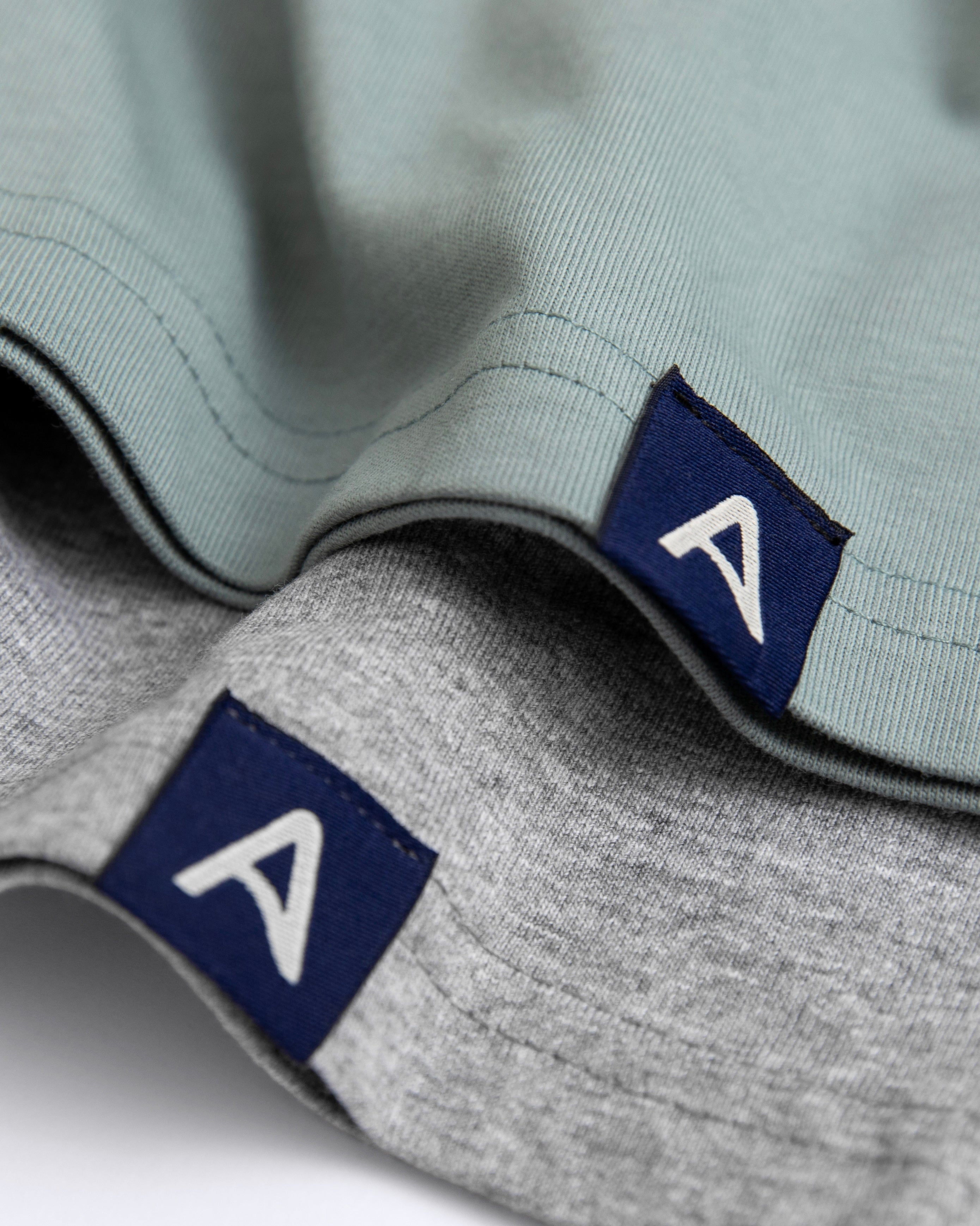 Close-up of two Avelamer Ebbtide tees with blue A-flag logo woven hem labels
